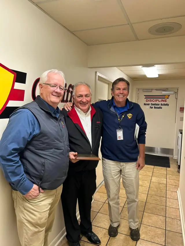 Three Certified Alarm team members holding a plaque in the office hallway